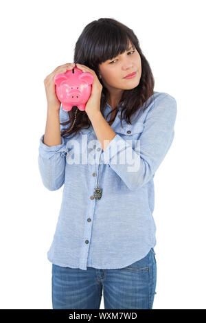 Junge Frau schüttelt ihr Sparschwein auf weißem Hintergrund Stockfoto