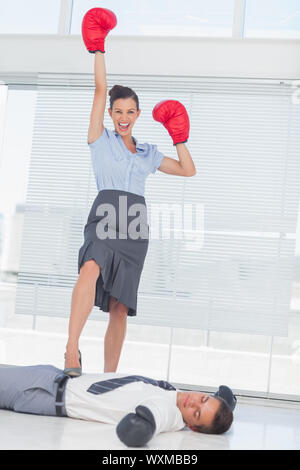 Geschäftsfrau, stehend auf besiegt Geschäftsmann tragen Boxhandschuhe in helles Büro Stockfoto
