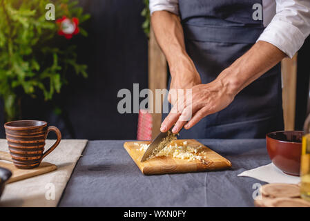 Ein männlicher Chef in einer schwarzen Schürze bereitet eine Weihnachten Teller durch Schneiden Knoblauch auf ein Schneidebrett. Freudige kochen für festliche Silvester und Weihnachten Tabelle Stockfoto