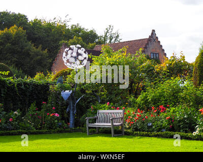 Chenies Manor Garden übersicht Löwenzahn Skulptur von Jenny Pickford. Der Pavillon ist im Hintergrund.. Eine hölzerne Sitzbank wird von Dahlien umgeben. Stockfoto