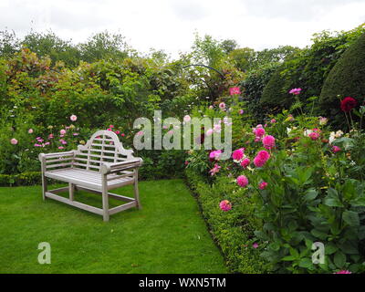 Sitz in der Ecke Chenies Manor Garden, Buckinghamshire, im Sommer Stauden Pflanzen, Dahlien und Kosmos umgeben. Stockfoto