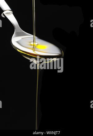 Olivenöl auf einem Löffel über schwarzen Hintergrund gegossen Stockfoto