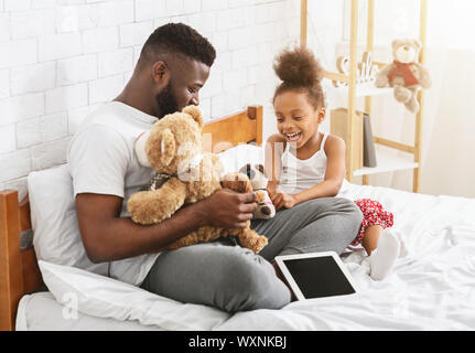 Fröhliche afro Mädchen Spielzeug spielen mit ihr Papa, sitzen auf dem Bett Stockfoto