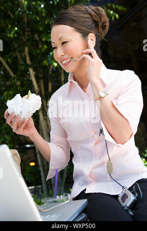 Junge Frau, mit mobilen während des Essens sandwich Stockfoto