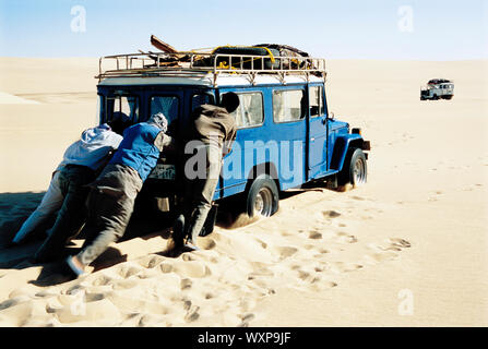 Männer schieben Jeep in die Wüste Stockfoto