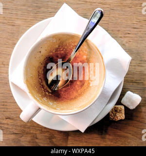 Auf der Suche nach einem leeren verwendet Tasse Cappuccino mit einem Löffel und Zwei von Würfelzucker auf einem Tisch Stockfoto