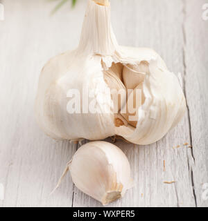 Single frischer Knoblauch Glühbirne kaputt öffnen die einzelnen Zehen mit einer Nelke im Vordergrund bei einer lackierten Oberfläche in Weiß zeigen Stockfoto