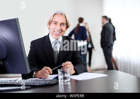 Closeup Portrait zufrieden zuversichtlich Geschäftsmann sitzt in seinem Büro mit Kollegen chatten im Hintergrund Stockfoto