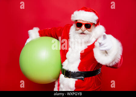 Holly Jolly merry x mas heiter Lustig positive stilvolle Santa in Brillen Handschuhe Pelzmantel schwarzen Gürtel tragen grüne Kugel, die auf der Kamera Stockfoto