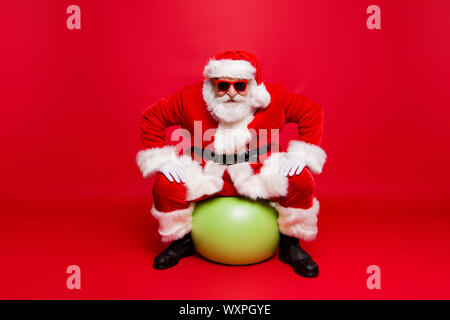 Lustig positive Elegante modische Santa in Brillen Handschuhe Pelzmantel winter Outfit Black Belt sitzen auf grüner Ball bereit zum Verkauf bereit Promo Stockfoto