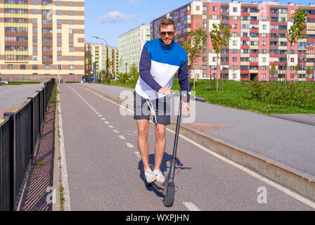 Sportlicher Kerl treibt moderne scooter im City Park Stockfoto