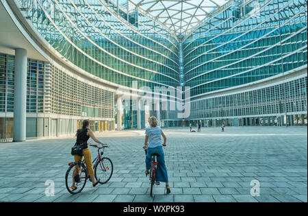 Mailand Italien - Juli 2019 zwei Frauen erkunden die Stadt mit dem Fahrrad abstrakten Strukturen eines modernen Gebäudes Glas Stockfoto