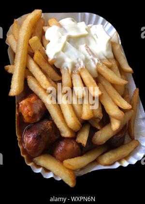 Currywurst & Pommes auf schwarzem Hintergrund: Berühmte deutsche Fast Food (Currywurst mit Pommes Frites und Curry Sauce) mit Ketchup und Mayonaise Stockfoto