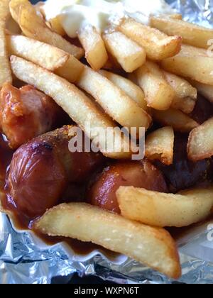 Currywurst & Pommes: Berühmte deutsche Fast Food (Currywurst mit Pommes Frites und Curry Sauce) mit Ketchup und Mayonaise auf Aluminiumfolie Stockfoto