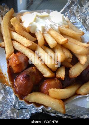 Currywurst & Pommes: Berühmte deutsche Fast Food (Currywurst mit Pommes Frites und Curry Sauce) mit Ketchup und Mayonaise auf Aluminiumfolie Stockfoto