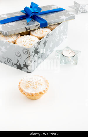 Mince Pies in cookie Zinn und auf weißem Hintergrund mit Teelicht und Weihnachten Dekoration. Stockfoto