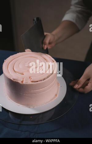 Mädchen Konditor, macht eine Hochzeitstorte mit seinen eigenen Händen und drückt auf die Sahne auf der Torte Schichten. Kopieren Sie Platz. Selektive konzentrieren. konditor Macht Stockfoto