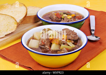 Zwei Zinn Schalen in einer Reihe mit hausgemachten Gemüse und Rindfleisch Suppe gefüllt. Es ist mit geröstetem Brot serviert. Stockfoto