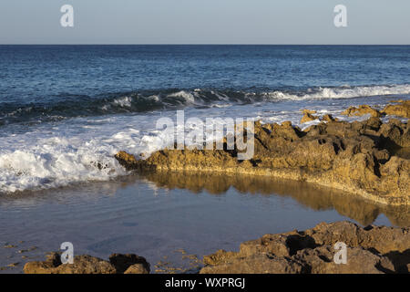 Schäumenden Wasser des blauen Ozean auf felsigen Strand erleuchtet von Goldenen Stunde. Stockfoto