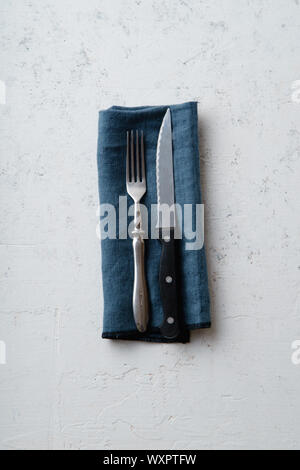 Messer und Gabel auf Blau textil Serviette auf Beton Stein Hintergrund Stockfoto