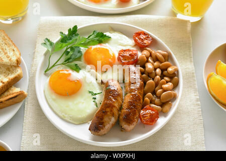 Frühstück mit Spiegelei, Würstchen, Bohnen, Tomaten, Grüns auf Platte Stockfoto