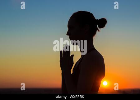 Sportliche Frau Yoga im Park bei Sonnenuntergang - Hand Gruß Namaste. Abendlicht, goldene Stunde, Lens Flares. Freiheit, Gesundheit und Yoga co Stockfoto