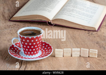 Ein Buch und eine Tasse Kaffee auf einem Holztisch mit kleinen Würfel mit Kopie Raum Stockfoto