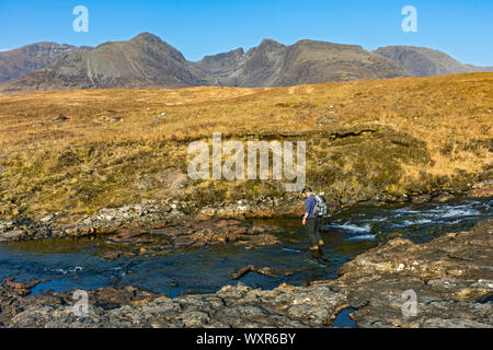 Walker Überquerung des Allt Coire Lagan Stream mit dem Cuillin Berge hinter, auf der Strecke zu Rubha eine Dùnain, Minginish, Isle of Skye, Schottland, Großbritannien Stockfoto