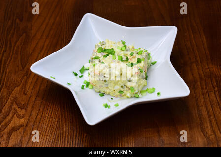 Olivie Salat in Weiß Platte in Form von Star. Traditionelles Gericht im Restaurant - Olivie Salat, Holz- Hintergrund. Restaurant Dish Konzept. Sa Stockfoto