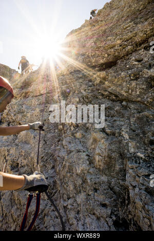 Gruppe von Bergsteigern auf einem vertikalen Klettersteige in den Dolomiten mit einem Sun Star in hellen goldenen Licht Stockfoto