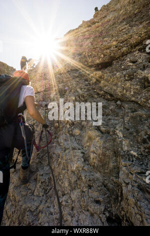 Gruppe von Bergsteigern auf einem vertikalen Klettersteige in den Dolomiten mit einem Sun Star in hellen goldenen Licht Stockfoto