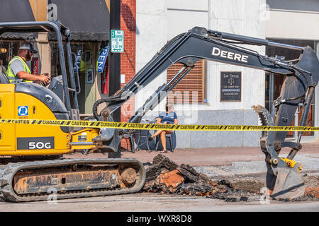 HICKORY, NC, USA-13 SEPT 2019: John Deere Traktor mit Tieflöffel bricht, Straße, Bürgersteig, während eine Frau Fuß weg entspannt auf einem Bürgersteig Tabelle. Stockfoto