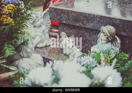 Blumenstrauß aus weißen Blumen und Engel Figuren während christliche Allerheiligen Veranstaltung liegt im Grab auf dem Friedhof Stockfoto