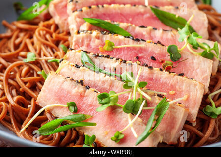 Japanische Soba-Nudeln Buchweizen mit in Scheiben geschnittenen Thunfisch mit Sesam auf dunklen Holztisch Stockfoto