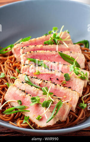 Japanische Soba-Nudeln Buchweizen mit in Scheiben geschnittenen Thunfisch mit Sesam auf dunklen Holztisch Stockfoto