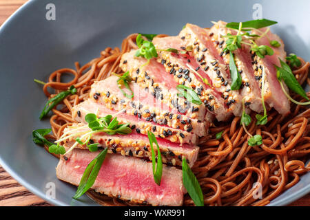 Japanische Soba-Nudeln Buchweizen mit in Scheiben geschnittenen Thunfisch mit Sesam auf dunklen Holztisch Stockfoto