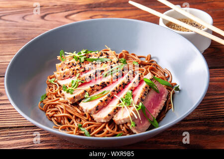 Japanische Soba-Nudeln Buchweizen mit in Scheiben geschnittenen Thunfisch mit Sesam auf dunklen Holztisch Stockfoto