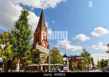 Die neo-gotischen Warnemünder Kirche Turm erhebt sich über die Altstadt von Rostock, Deutschland, als Touristen und Deutsche speisen Sie auf der Terrasse im Freien Platz. Stockfoto