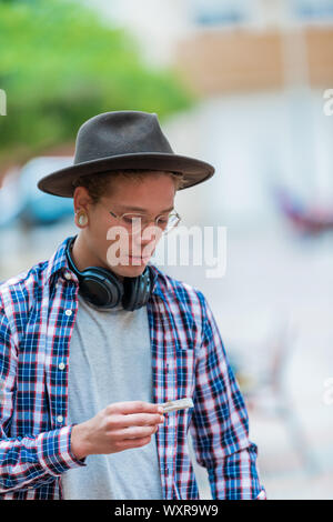 Porträt eines weißen Jungen in einem Quadrat Shirt und einen schwarzen Hut gekleidet, halten mit der einen Hand eine Zigarette, den Hintergrund unscharf. Künstler junge Konzept. Stockfoto