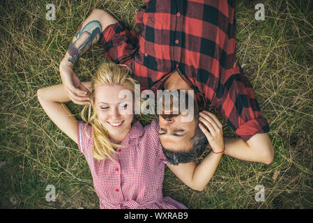 Junges Paar in der Liebe. Zwei Menschen, blondes Mädchen und bärtiger Mann, liegend auf grünem Gras. Freundin und Freund spielt mit jeden anderen Haar. Stockfoto