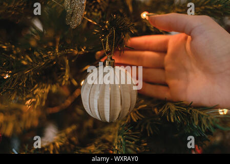 Ein Mann hängt ein Weihnachten Spielzeug auf ein Neues Jahr Baum mit einer Girlande. Stockfoto