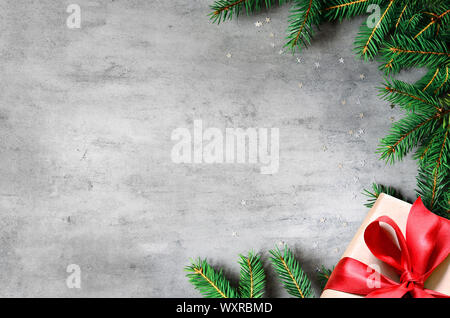 Weihnachtsgeschenke mit roter Schleife auf grauem Hintergrund in einem Rahmen aus Tannenzweigen. Flach, Ansicht von oben. Weihnachten Hintergrund. Stockfoto