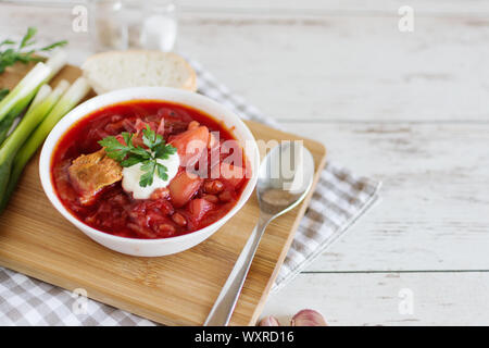 Traditionelle ukrainische und russische Küche, Suppe mit Rüben und Tomaten zubereitet. Ein weißer Teller mit Rote-Bete-Suppe auf Holz- Hintergrund. Stockfoto