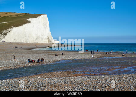 Tagesausflügler am Strand von Cuckmere Haven, in der Nähe von Eastbourne, East Sussex UK, mit Kreidefelsen im Hintergrund Stockfoto