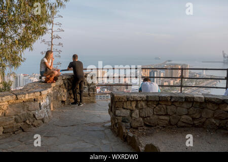 Touristen am Aussichtspunkt Gibralfaro mit Blick auf den Hafen von Malaga en Stadt, bei Sonnenuntergang, Andalusien, Spanien. Stockfoto