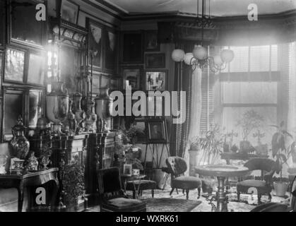 AJAXNETPHOTO. 1922. AGRA, Indien. - Koloniales Interieur - WOHNZIMMER EINES KOLONIALEN RESIDENCE GEFÜLLT MIT ARTEFAKTEN, darunter Gemälde, Schmuck, kurzes Bein Stühle, Tische und Topfpflanzen. Foto: T.J. SPOONER COLL/AJAX VINTAGE BILDARCHIV REF; 1922 104 Stockfoto