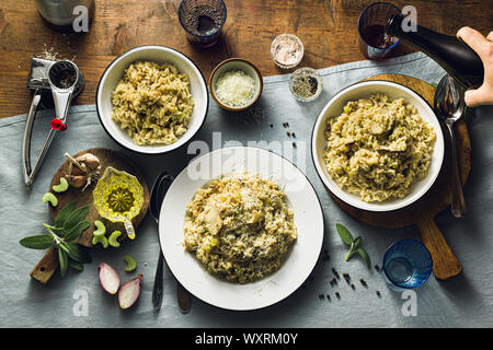 Klassische italienische Risotto mit Pilzen auf einem Holztisch mit einem blauen Leinen Tischdecke. Rotwein. Flasche und Gläser. top Shots, männliche Hand gießt Wein Stockfoto