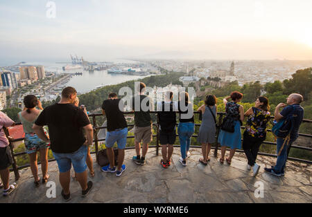 Touristen am Aussichtspunkt Gibralfaro mit Blick auf den Hafen von Malaga en Stadt, bei Sonnenuntergang, Andalusien, Spanien. Stockfoto