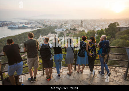 Touristen am Aussichtspunkt Gibralfaro mit Blick auf den Hafen von Malaga en Stadt, bei Sonnenuntergang, Andalusien, Spanien. Stockfoto