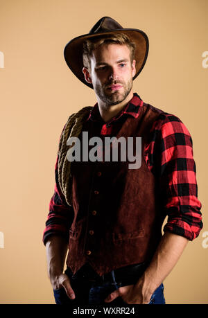 Unrasierten Kerl in Cowboyhut. Schöne bärtige Macho. Cowboy Hut tragen. American Cowboy. Schönheit Standard. Beispiel wahrer Männlichkeit. Westliche leben. Mann unrasiert Cowboy beigen Hintergrund. Stockfoto